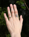 Hand wearing a ring with a geometric tattoo on the other finger against a dark background