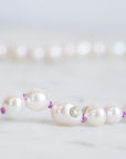 Pearl necklace with purple accents on a light gray background