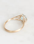 A yellow gold ring featuring a light blue gemstone and small clear accent stones, photographed on a light gray background.