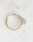 A gold ring with a small gemstone and tiny clear accent stones, photographed on a pale marble-like surface.