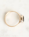 A gold ring with a dark gemstone and two small clear accent stones, photographed on a light marble-like surface.