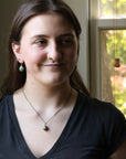 Woman wearing a black top and necklace with a blurred window background