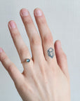 Hand wearing a ring with a small gemstone on a plain background