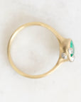 A gold ring with a green marquise-cut center stone and three small clear accent stones, photographed from above on a light marble surface.