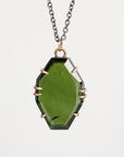 A faceted green gemstone pendant necklace with a dark metal chain and gold-toned prong settings, shown against a light gray background.