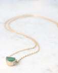 Gold necklace with a green gemstone pendant on a white marble surface