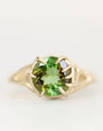 A yellow gold ring featuring a round-cut green gemstone in a prong setting, shown against a plain white background.