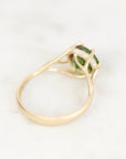 A yellow gold ring featuring a green rectangular gemstone in a prong setting with small clear accent stones, shown on a light marble background.