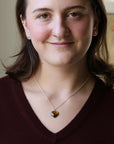 A woman with brown hair wearing a silver chain necklace with a heart-shaped amber gemstone pendant, paired with a burgundy V-neck sweater.