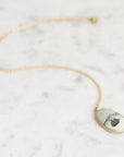 Necklace with a gold chain laid out. The pendant is a white stone with a ship engraving on it.