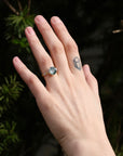 Large green sapphire ring with lots of barnacles on hand with tattoo against natural background