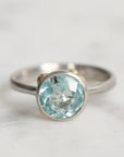 Silver ring with a light blue gemstone on a light gray background