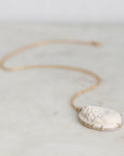 A delicate gold chain necklace featuring an off-white carved shell pendant, resting on a light marble surface.