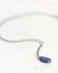 Opal necklace with gold prongs and oxidized silver chain laying on a marble background.