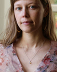 Woman wearing opal necklace and a floral blouse. She is looking at the camera, and set against an indoor background.