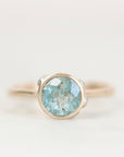 Blue bezel set gemstone ring with lots of inclusions against a plain background.