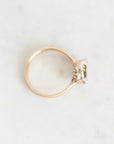 A gold ring with a small green rectangular gemstone and clear accent stones, photographed on a light marble surface.