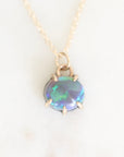 Purple opal set in yellow gold with a yellow gold chain against a plain backround.
