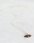 brown pendant on silver chain laying on gray background