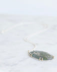Teardrop-shaped pendant with green stone on a white background
