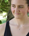 Woman wearing a black top and green earrings with a blurred natural background