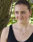Woman wearing a black tank top with a necklace, standing outdoors with greenery in the background