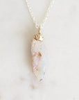 Light colored fossilized opal with gold rose detail suspended from a silver chain against a white background.