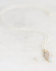 Light colored fossilized opal with silver chain and gold cap on a marble background.