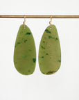 A pair of large, teardrop-shaped olive green resin drop earrings with green mineral inclusions, hanging from gold-tone fishhook ear wires on a horizontal brass rod against a white background.