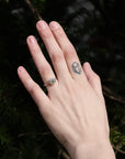 Hand with a ring and tattoo against a dark green leafy background
