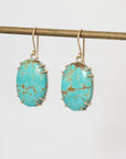 Turquoise earrings on a thin rod against a light gray background