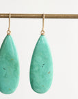 Teardrop-shaped turquoise earrings on a gold earring stand against a white background