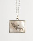Silver necklace with a square pendant featuring an engraved shark design on a white background