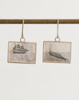 Pair of earrings with ship and whale illustrations on a white background