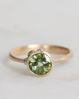 Gold ring with a green gemstone on a light gray background