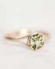 Gold ring with branchy prongs photographed from the side with a bright green gemstone.