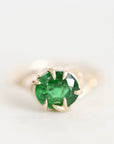 A round-cut green emerald gemstone ring set in a gold prong setting, photographed on a clean white background.