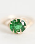 A round-cut green emerald gemstone ring set in a gold prong setting, photographed on a clean white background.