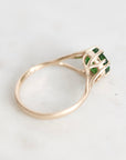 A gold ring with a green gemstone in a prong setting, photographed on a light marble surface.