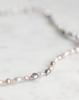 A delicate necklace featuring a mix of white, silver, and rose gold pearls threaded with small rose gold beads, displayed on a light marble surface.