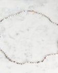 A delicate silver-toned beaded necklace with a small gold clasp, displayed on a white marble surface.