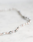 A close-up of a beaded strand necklace with mixed silver, white, and pale pink pearls on a light marble surface.