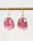 A pair of handmade dangle earrings featuring rough, faceted pink tourmaline stones in gold prong settings, hanging from gold fishhook wires against a clean white background.
