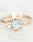 Light blue gemstone held in branchy gold prongs surrounded by diamond berries.