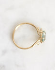 A gold ring with a small rectangular light green gemstone, photographed from above on a white marble surface.