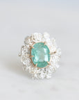 Glowing green stone held in gold prongs with a wreath of silver roses surrounding it