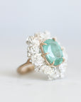 Side view of glowing green stone ring held in gold prongs with a wreath of silver roses surrounding it