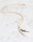 Necklace featuring a shark on a mother of pearl pendant suspended from a gold chain