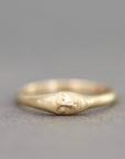 A small gold ring with a sculpted face motif on the band, photographed against a neutral gray background.