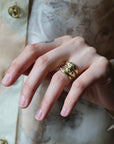 A close-up of a hand wearing three stacked gold rings, with a soft-focus background showing a patterned garment.